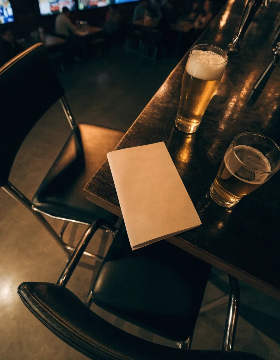 A folded menu card on a bar table between two drinks with chairs pushed back behind