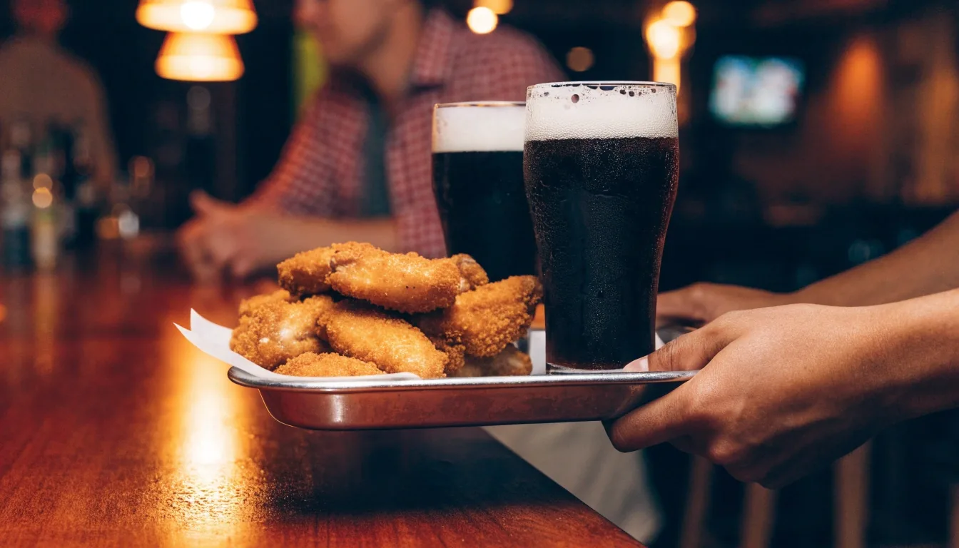 Bone-in wings on a bar liner beside a draft glass under warm lamp light